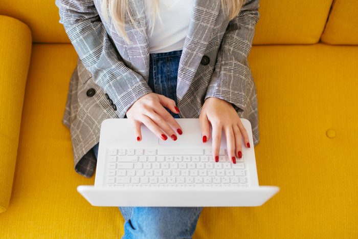 Business woman sitting on yellow couch, using laptop