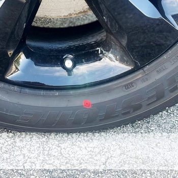 Tire displayed with red dot, showcasing branding and technical details, situated on a textured road surface.