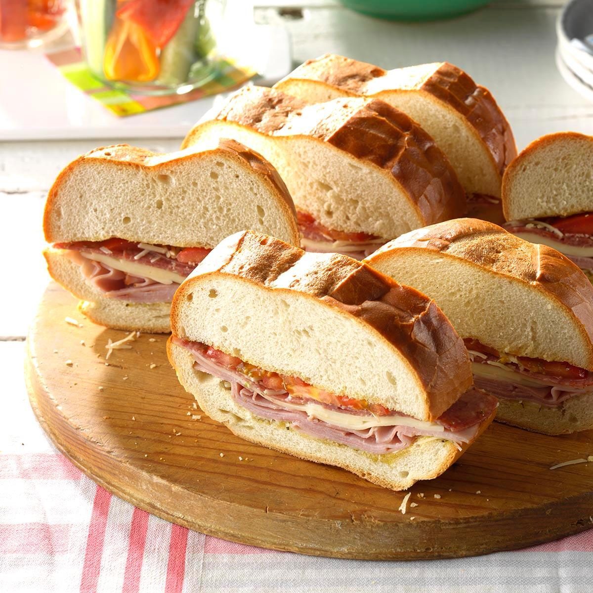 Sandwiches rest sliced on a wooden board, filled with meats and cheese, in a bright dining setting.