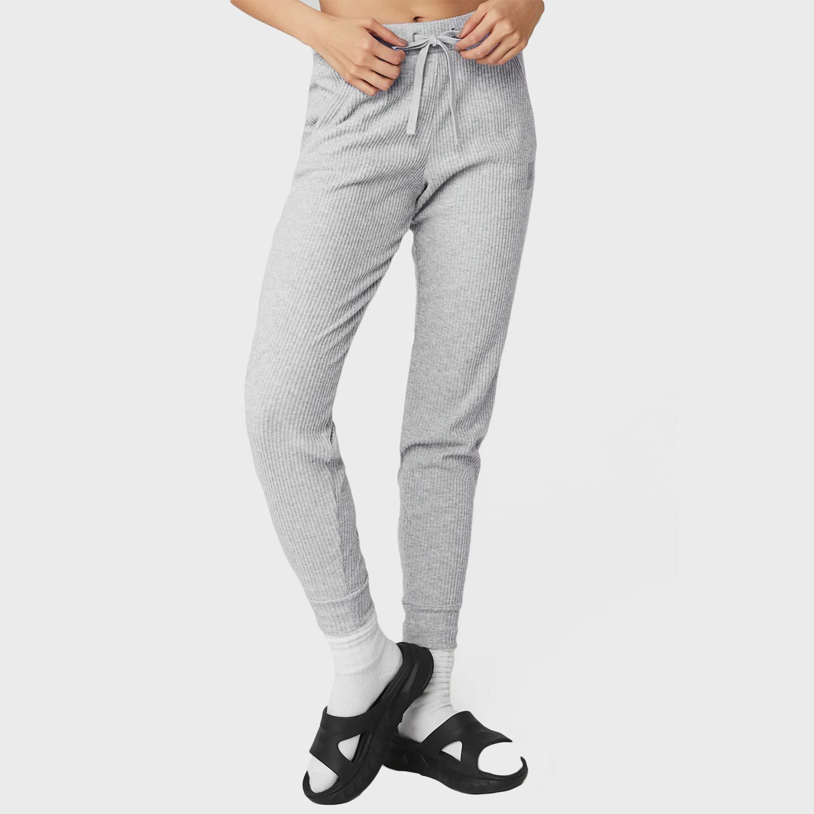 Gray joggers are worn by a person standing; the person is wearing white socks and black open-toe slides, with a plain white background.