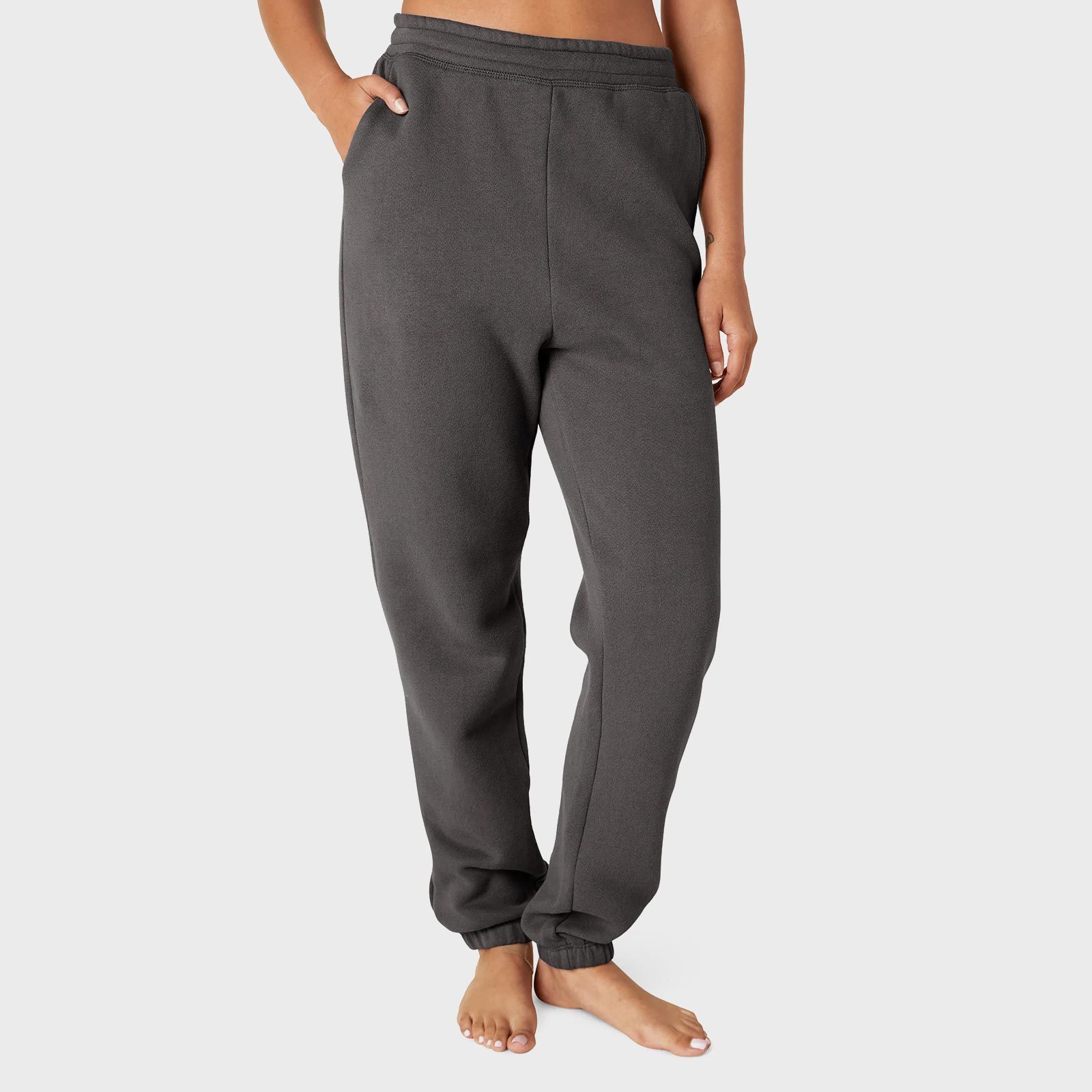 Gray sweatpants hang loose, worn by a person standing barefoot, one hand in pocket, against a plain light background.