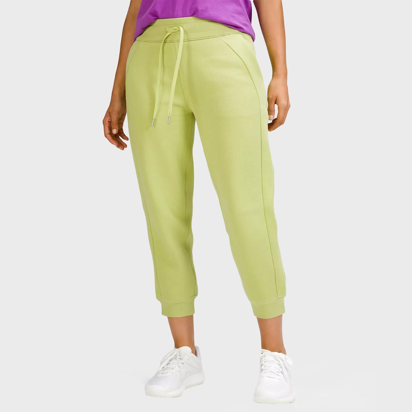 Person wears light green sweatpants and white sneakers, standing against a plain background, with a purple shirt partially visible.