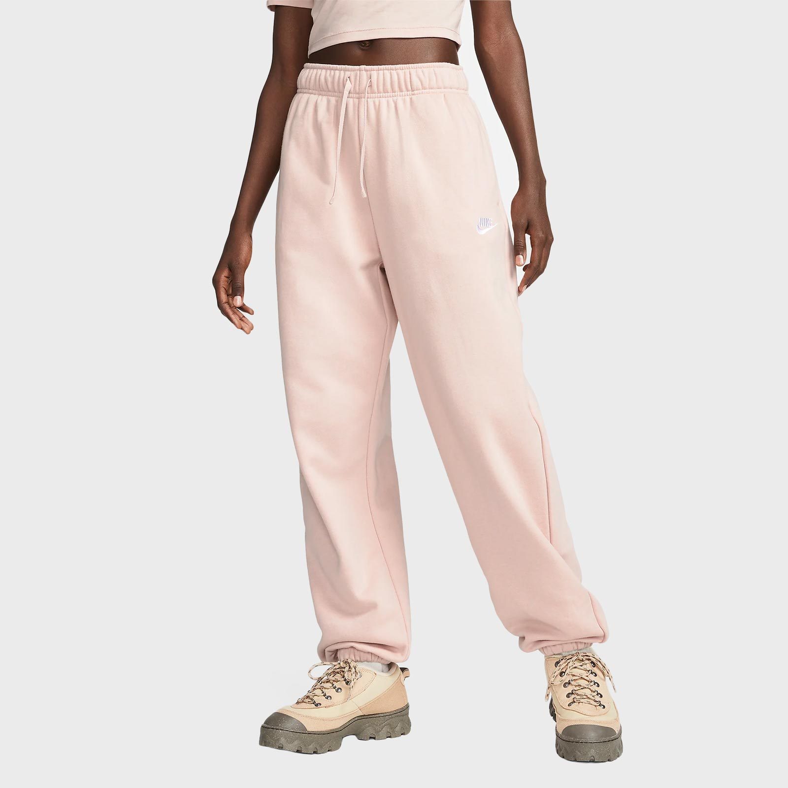 Person stands wearing pale pink sweatpants and tan hiking boots, positioned against a plain, light gray background.