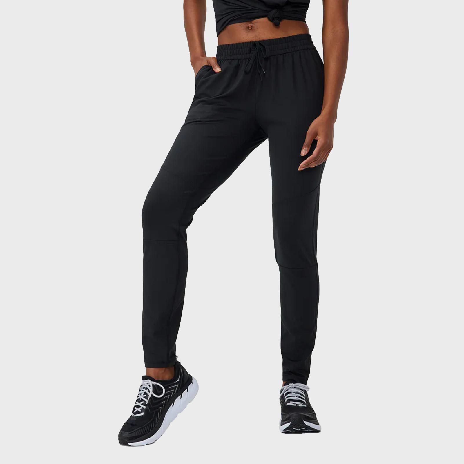 Person wearing black joggers stands casually, hands in pockets, in a neutral studio setting.