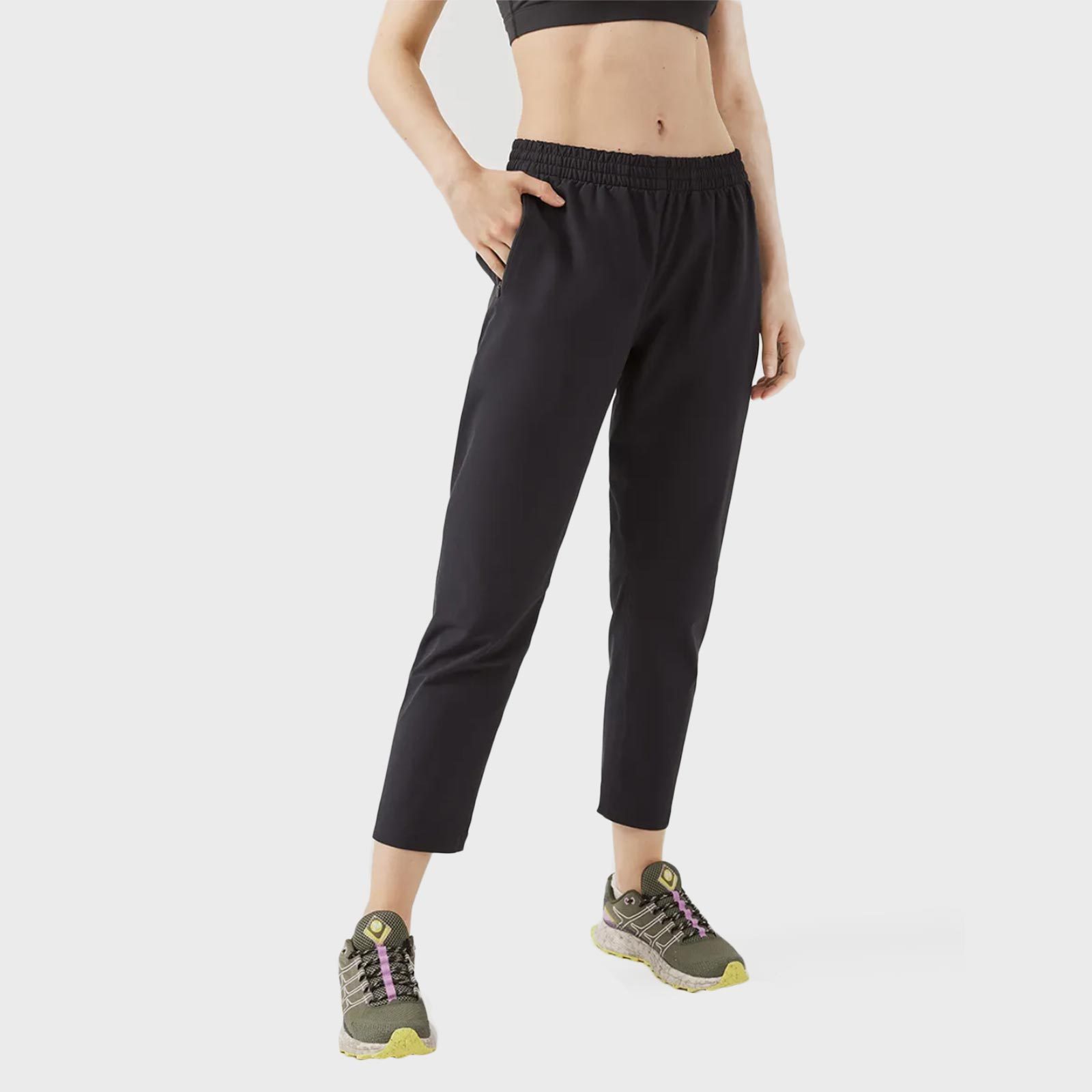 Person standing with hand in pocket, wearing black athletic pants and green sneakers, against a plain white background.