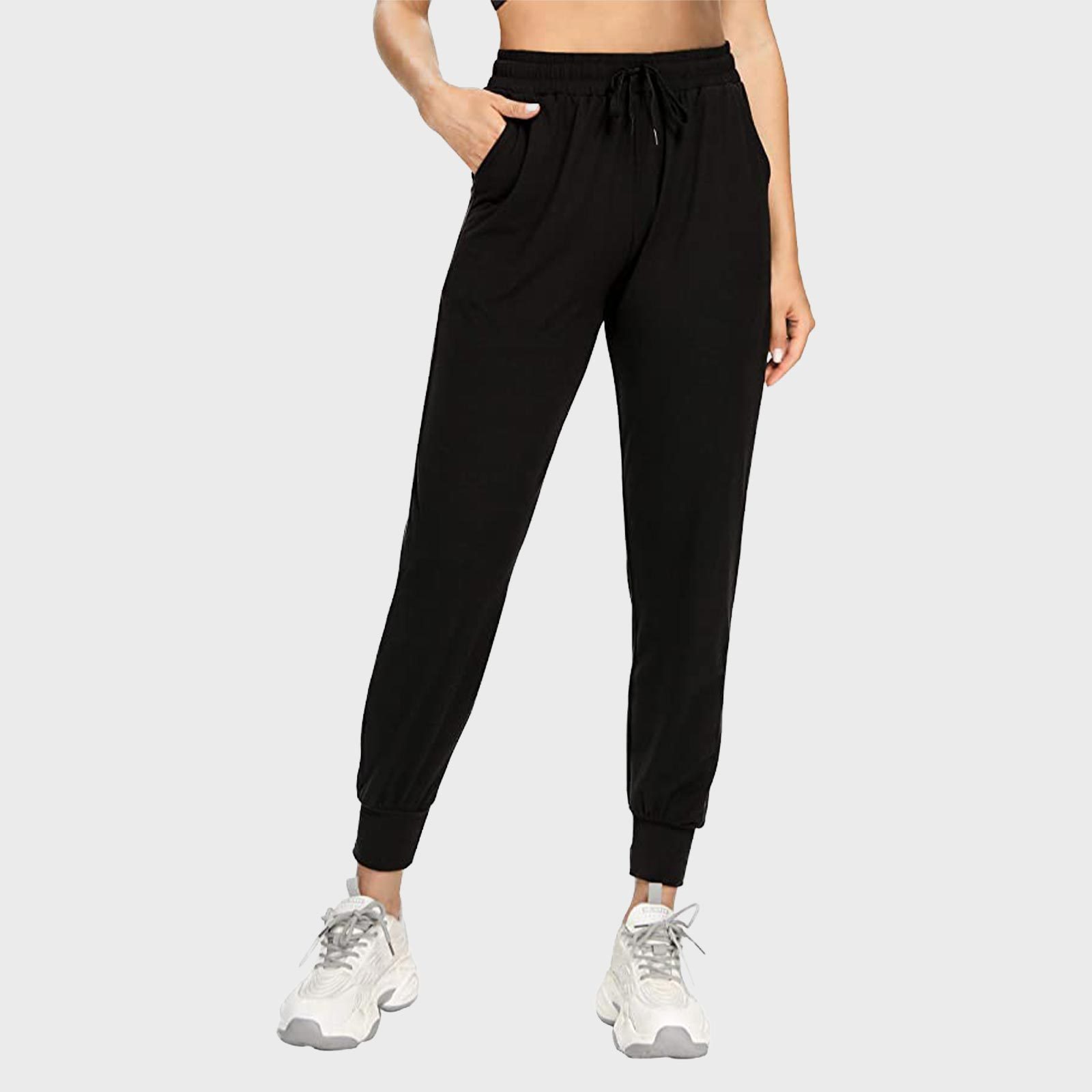 Black joggers with drawstring waistband worn by a person, featuring hands in pockets, paired with white sneakers against a plain gray background.