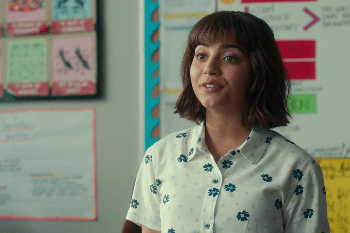 A person speaks in a room with educational posters and papers on the walls.