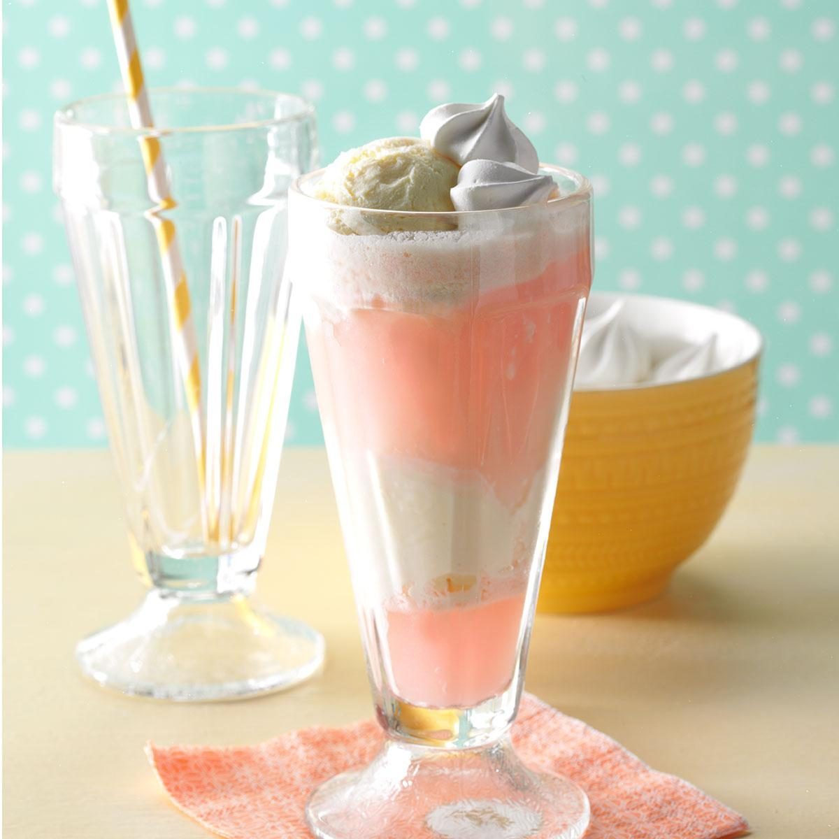 Milkshake sits in a tall glass, topped with ice cream and meringue, beside an empty glass with a straw and a yellow bowl.