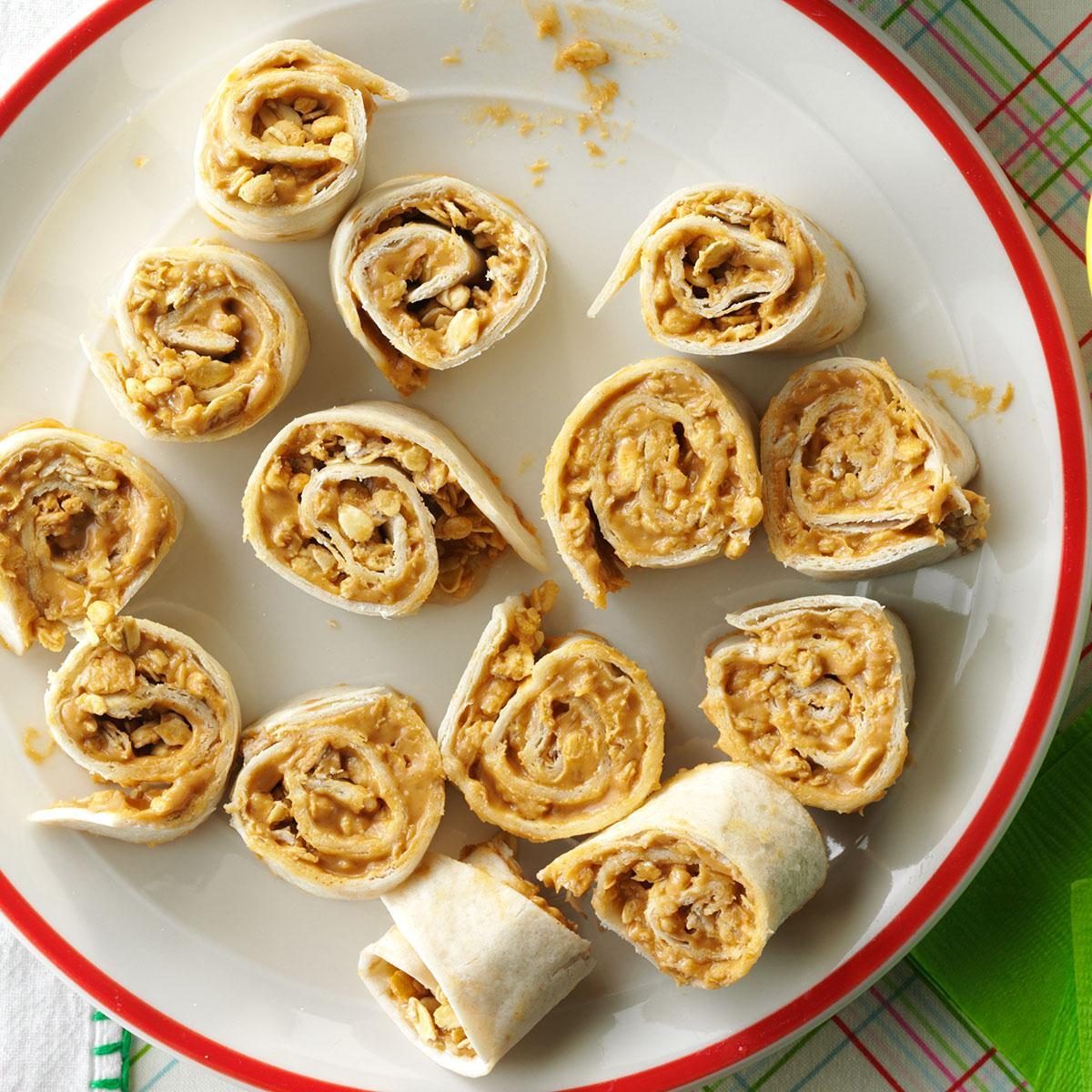 Pinwheel snacks with peanut butter filling arranged on a white plate with a red rim, placed on a plaid tablecloth.