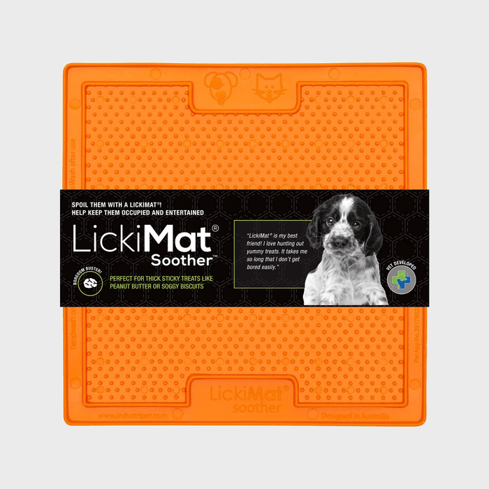 Orange pet mat with raised dots, designed for sticky treats. Black label features a dog photo and text promoting the 