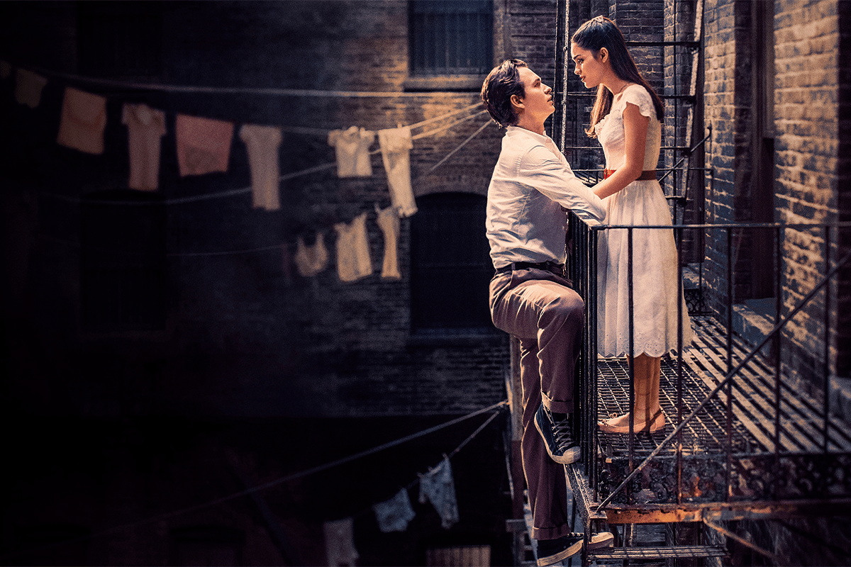 A couple gazes into each other's eyes on a fire escape, surrounded by hanging laundry, in a dimly-lit alley.