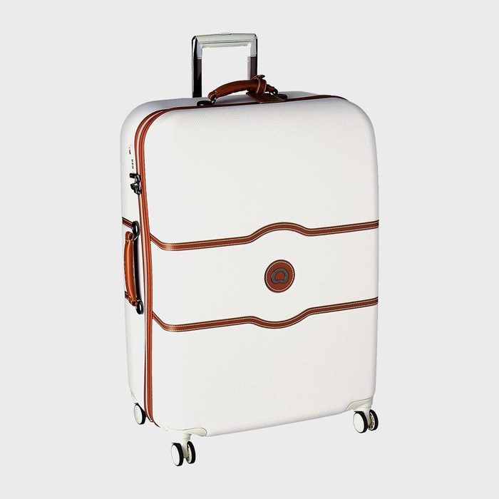 White suitcase standing, featuring brown leather accents and wheels, set against a plain gray background.