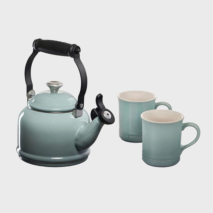 Teal kettle with black handle sits beside two matching mugs labeled 