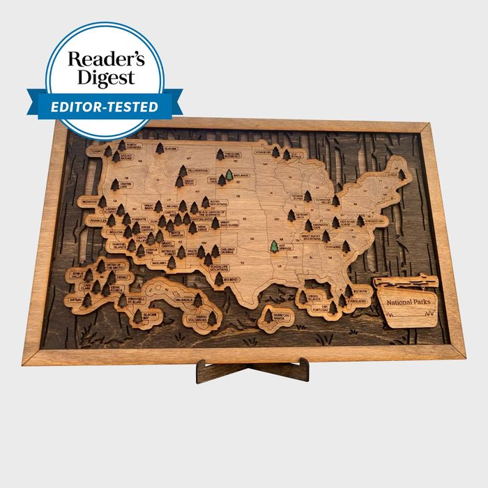 Wooden map highlights national parks, marked by icons, with a â€œReaderâ€™s Digest Editor-Testedâ€ badge above; framed and mounted on a stand.