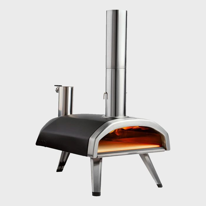 Pizza oven emits warm light, standing on metallic legs in a minimalistic setting.