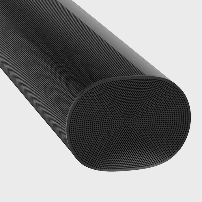 Black cylindrical speaker resting on a flat surface, featuring a perforated front grille design and a smooth, matte finish.