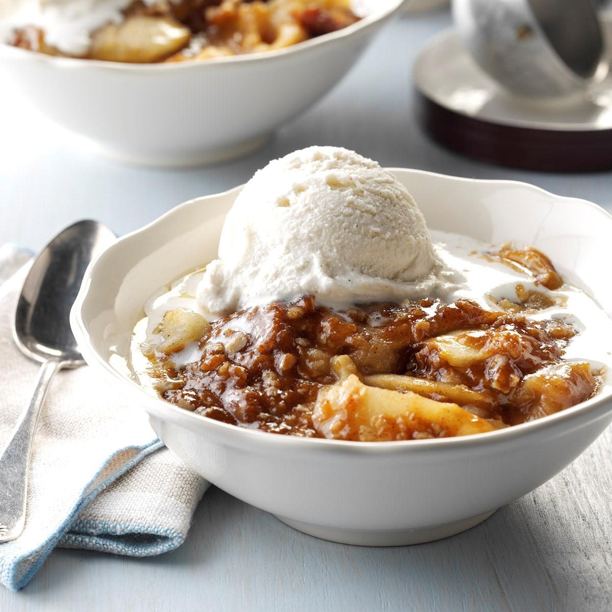 Bowl holds apple dessert topped with vanilla ice cream, resting on a table with spoon and napkin nearby.