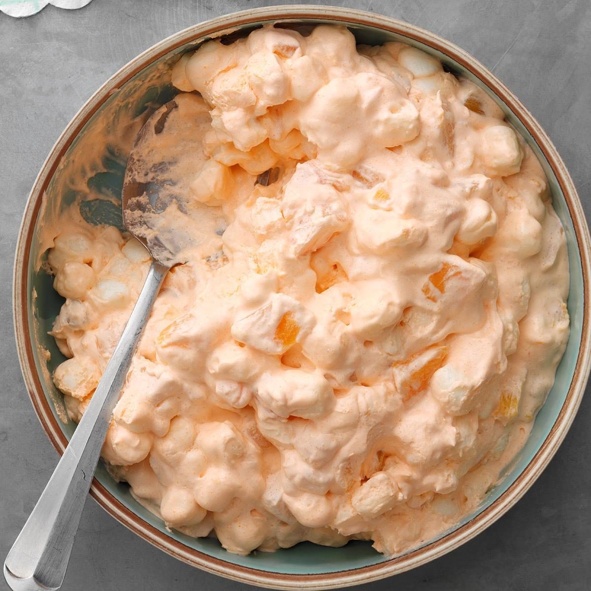 Fluffy orange dessert sits in a bowl with a spoon, resting on a gray surface.