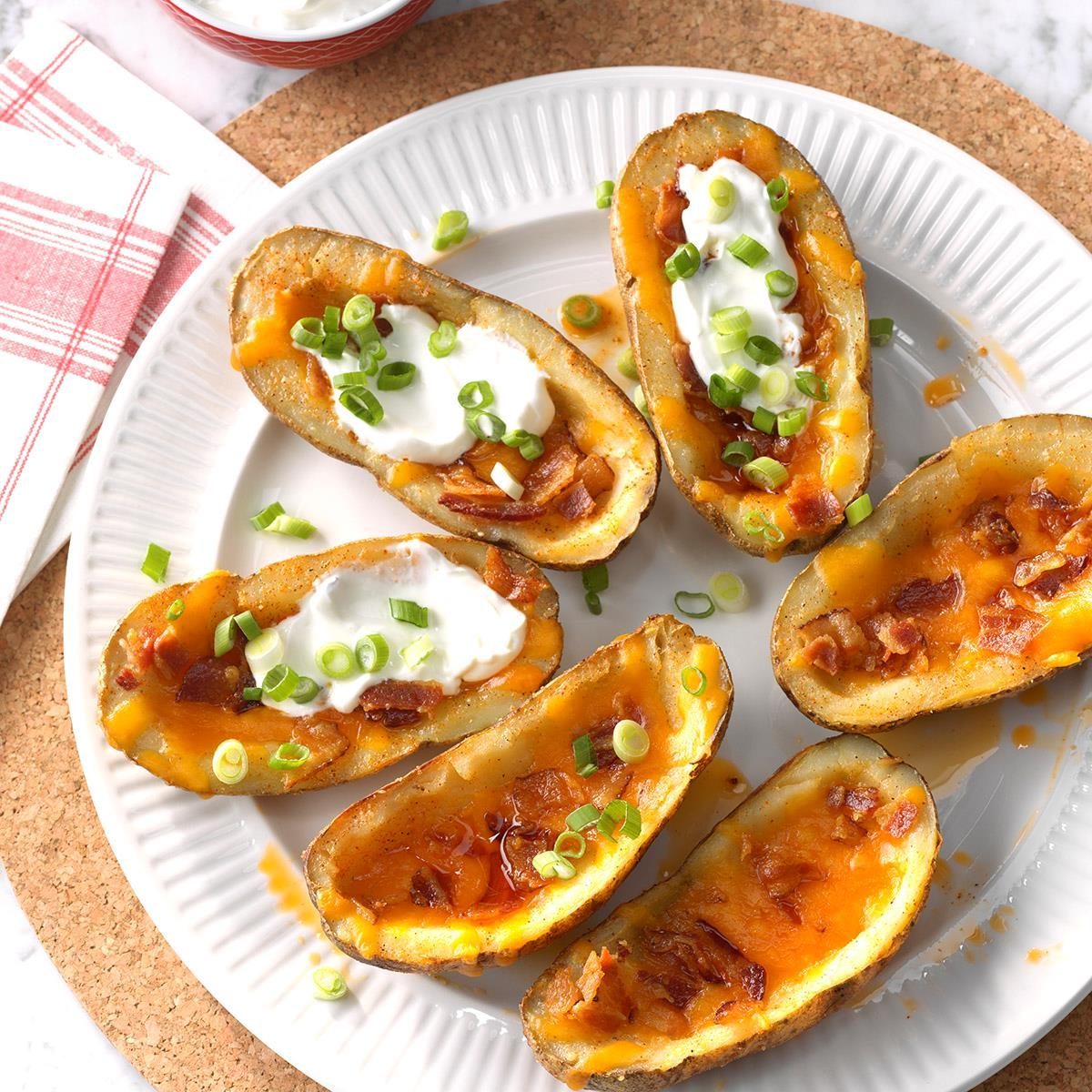 Potato skins hold melted cheese and bacon topped with sour cream and scallions, arranged on a white plate with a cloth napkin nearby.