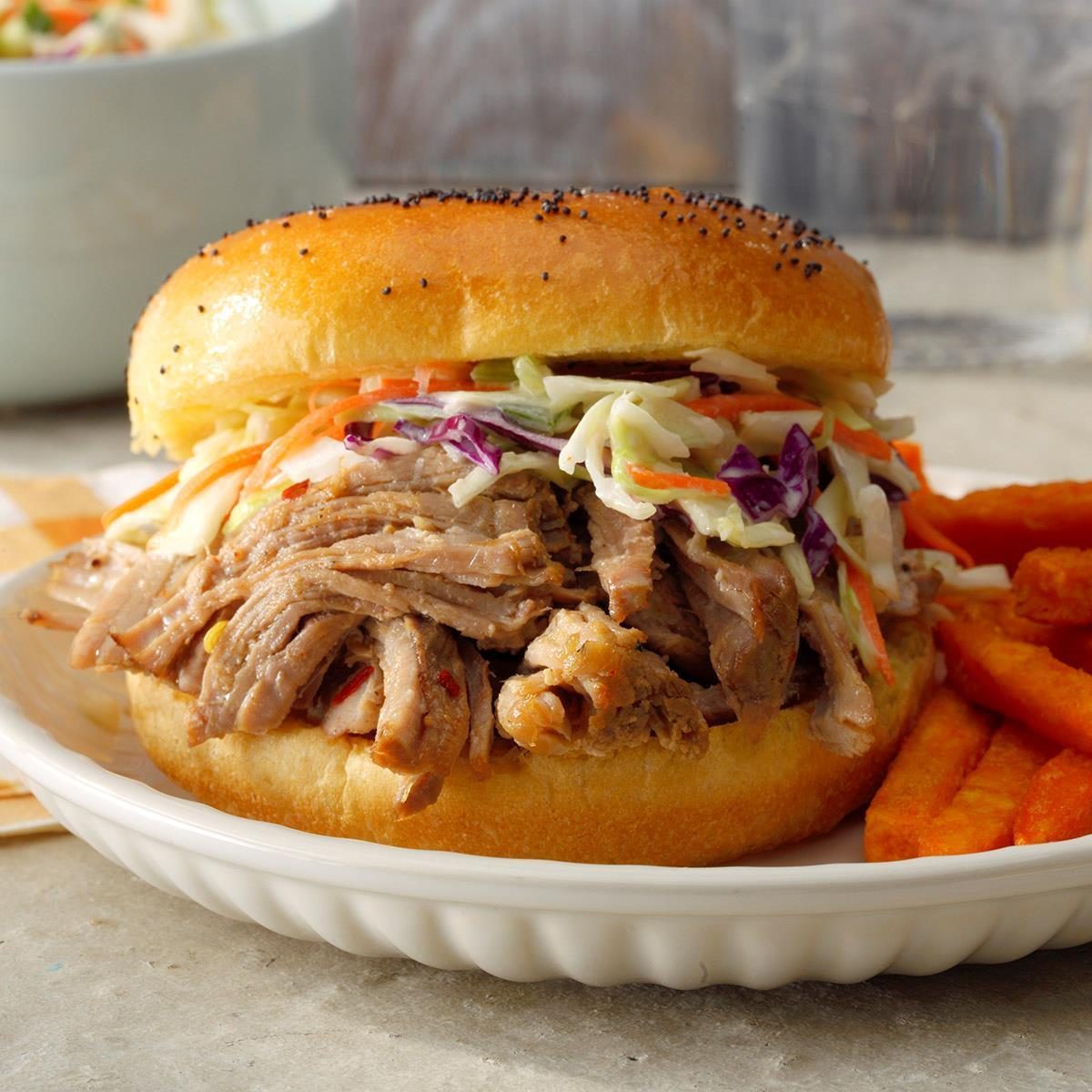 Pulled pork sandwich topped with coleslaw sits on a plate next to sweet potato fries.