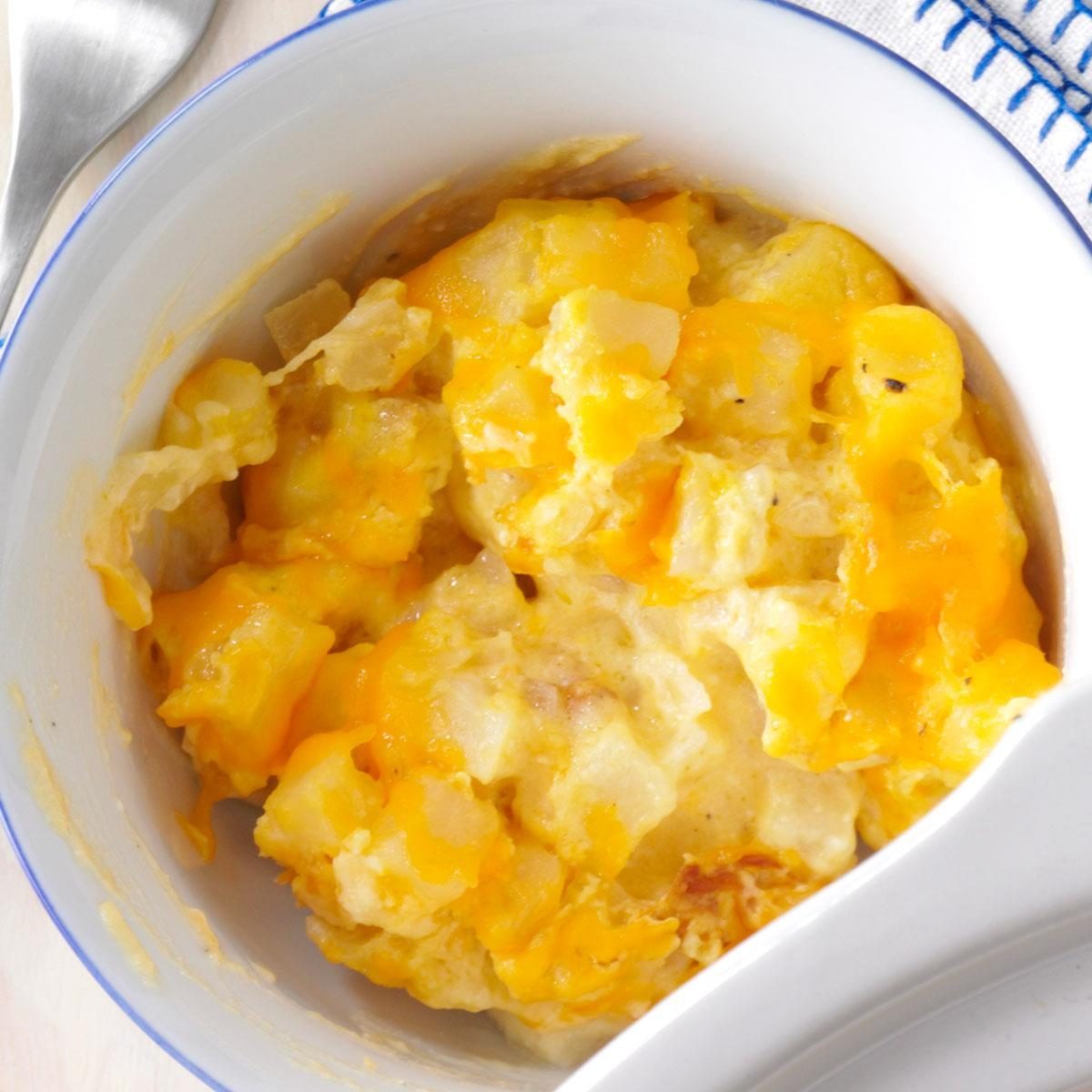Creamy, cheesy potatoes sit in a white bowl with a spoon nearby, resting on a patterned napkin.