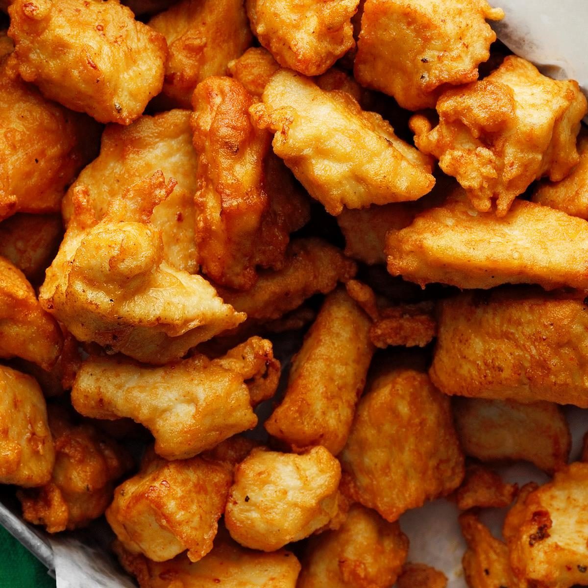 Golden-brown chicken nuggets clustered closely, resting on crinkled paper, suggesting a freshly prepared, appetizing snack setting.