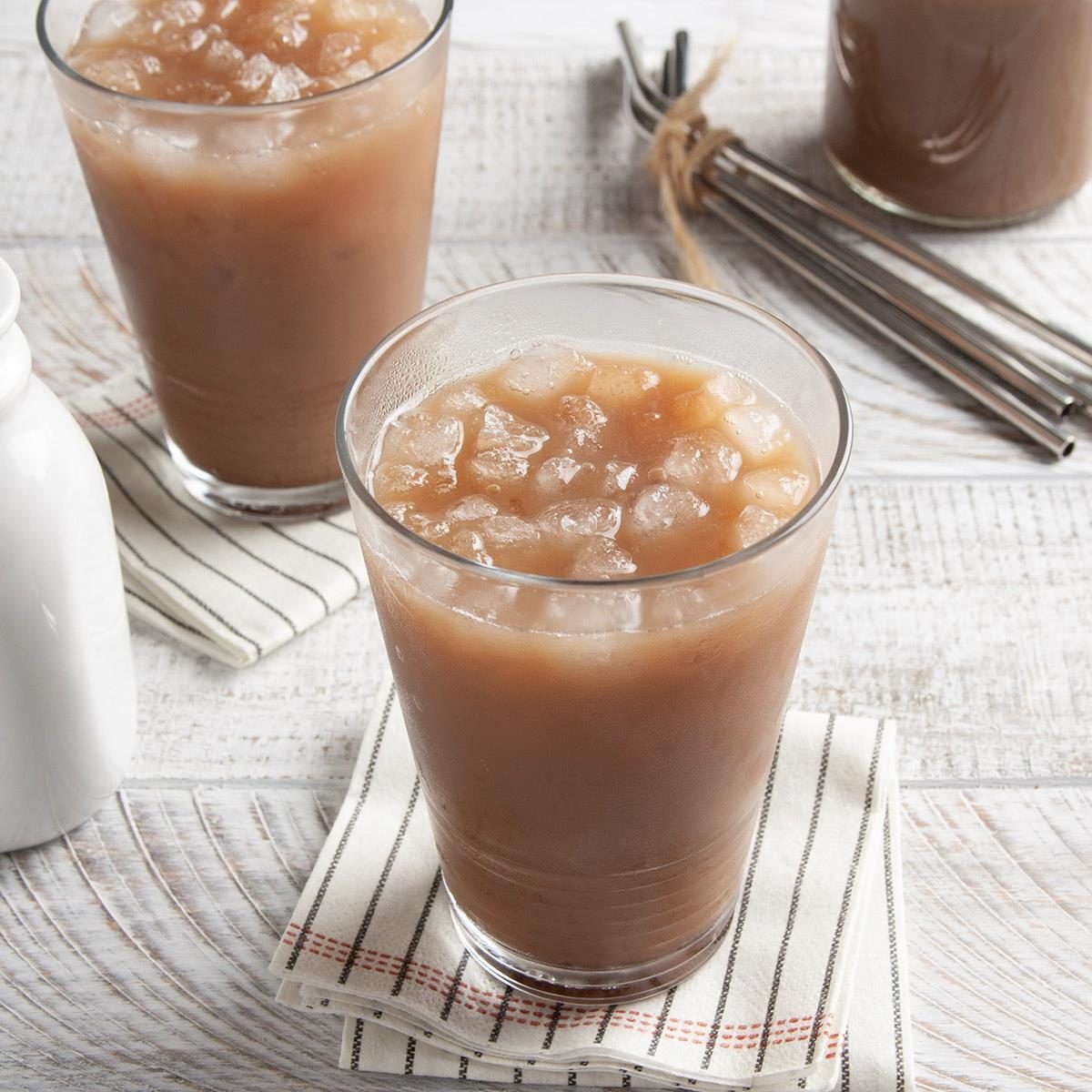 Iced coffee sits in glasses with ice cubes, resting on striped napkins on a white wooden table.