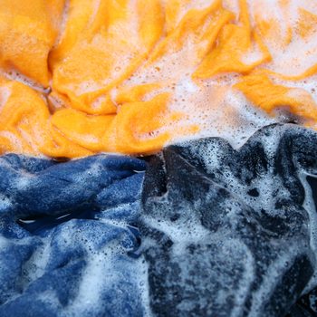 Colorful fabrics soak in soapy water, bubbles forming around them, creating a vibrant, textured surface.