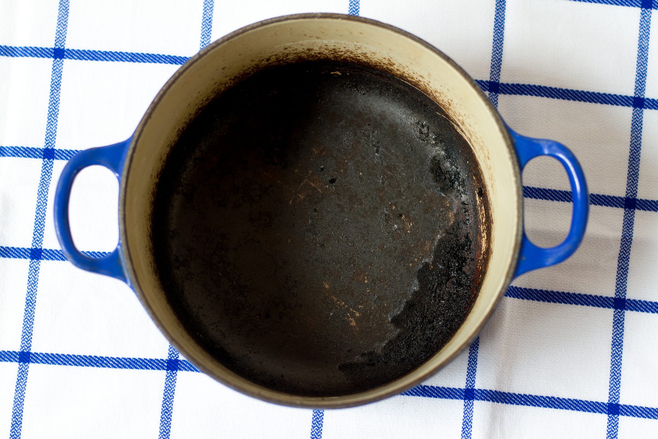 A burnt, empty pot sits on a white and blue checkered cloth.