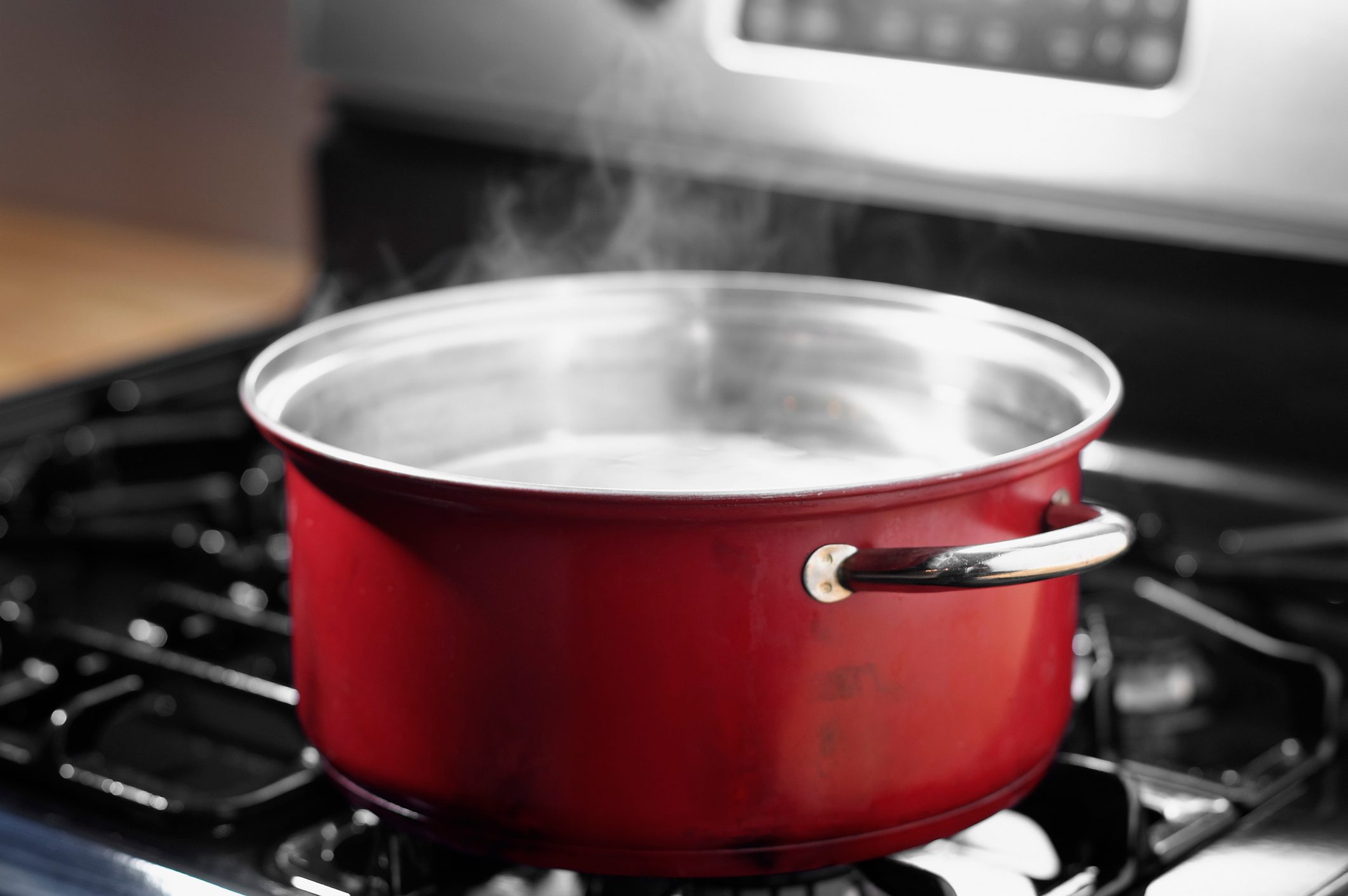 Red pot boiling water on a stove, emitting steam into a kitchen environment.