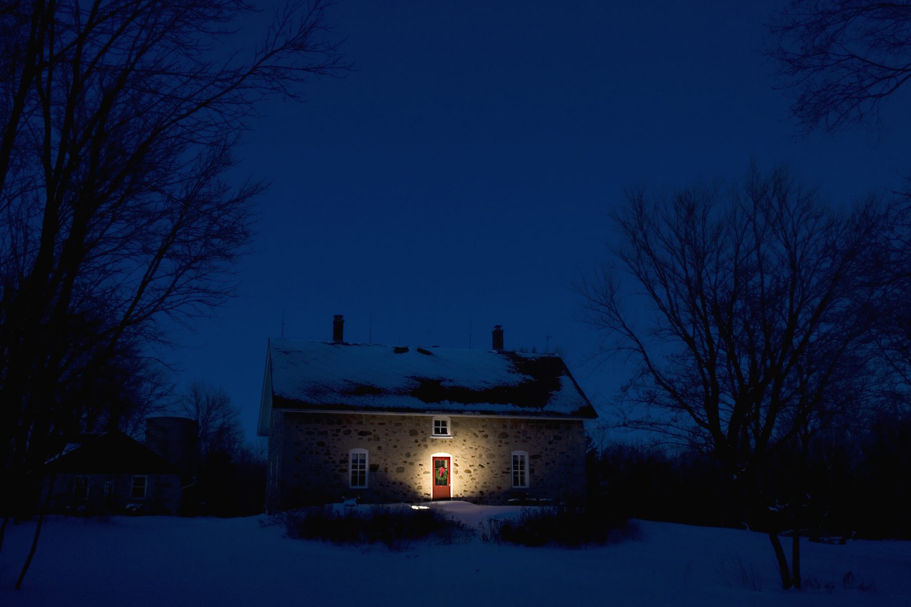 Illuminated Christmas wreath on door of stone house at dusk in Cedarburg, WI