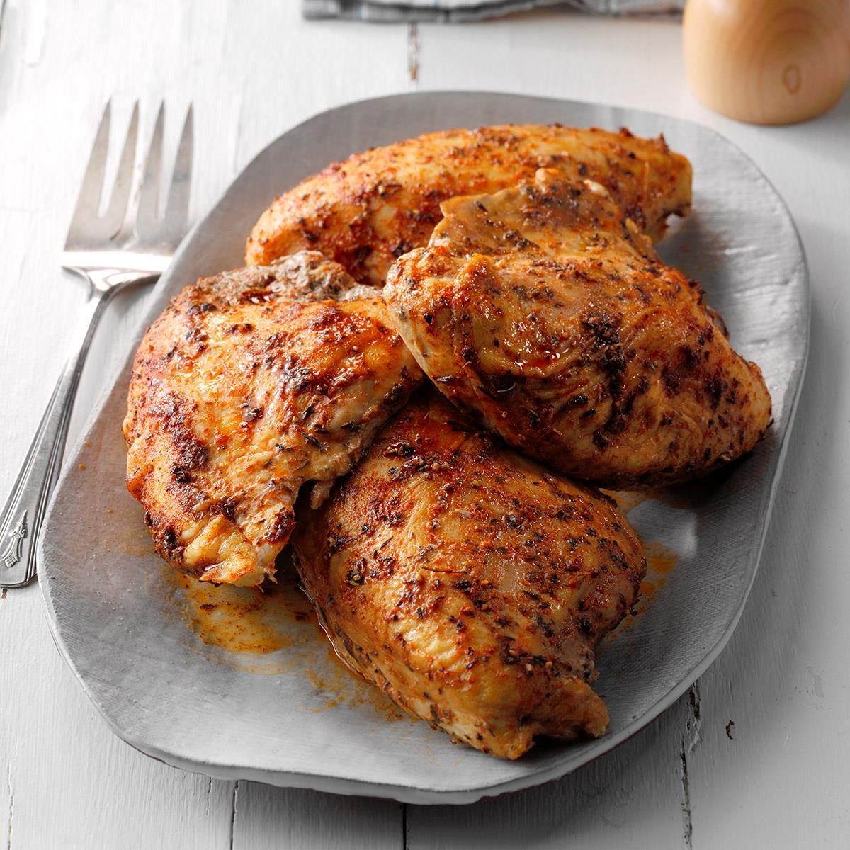 Roasted chicken breasts rest on a gray plate, surrounded by a fork on a white wooden table.