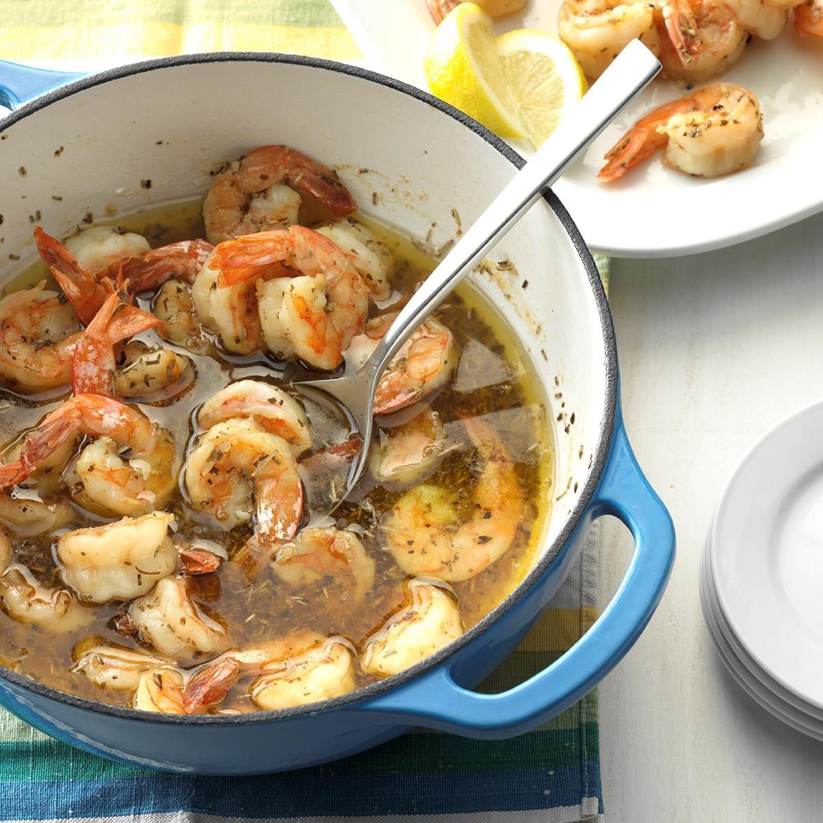 Shrimp simmer in seasoned broth inside a blue pot, surrounded by a table setting with lemon slices on a nearby plate.
