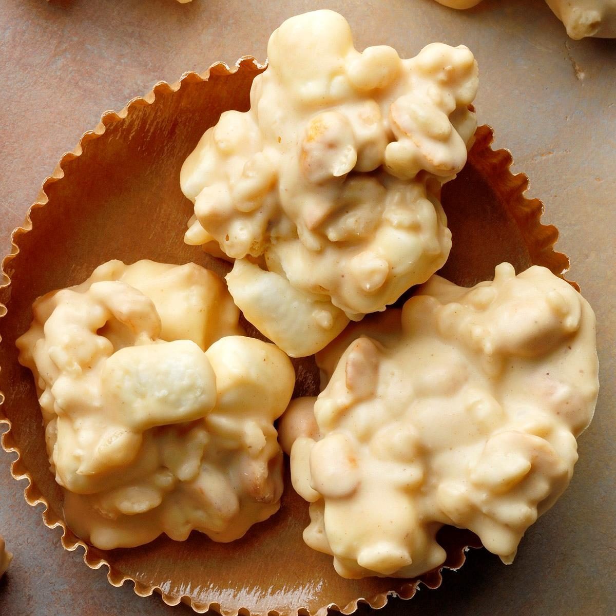 Clustered white chocolate morsels sit in a crinkled paper cup on a textured, light-colored surface.