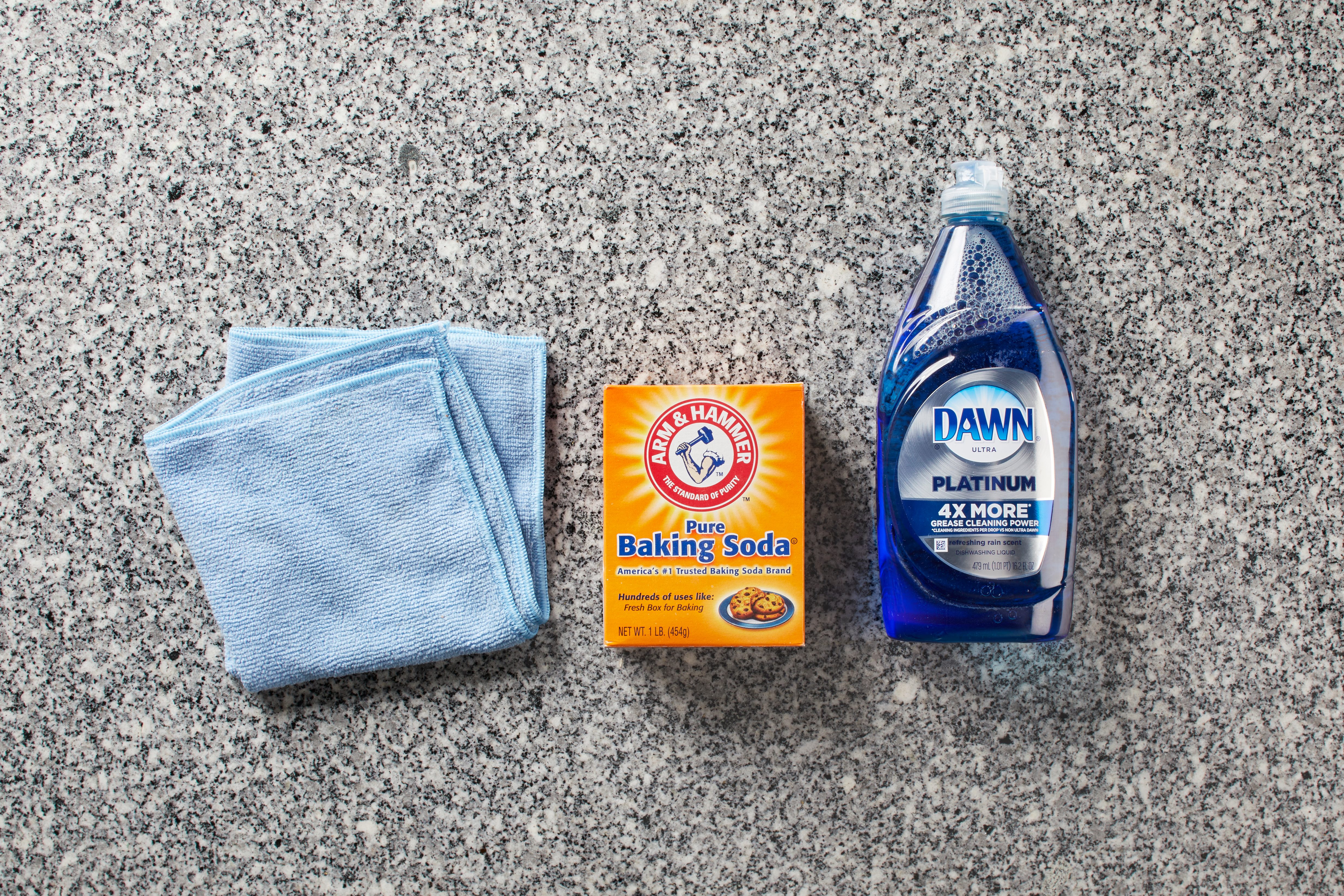 Blue cloths lie beside boxed baking soda and dish soap on a granite countertop.