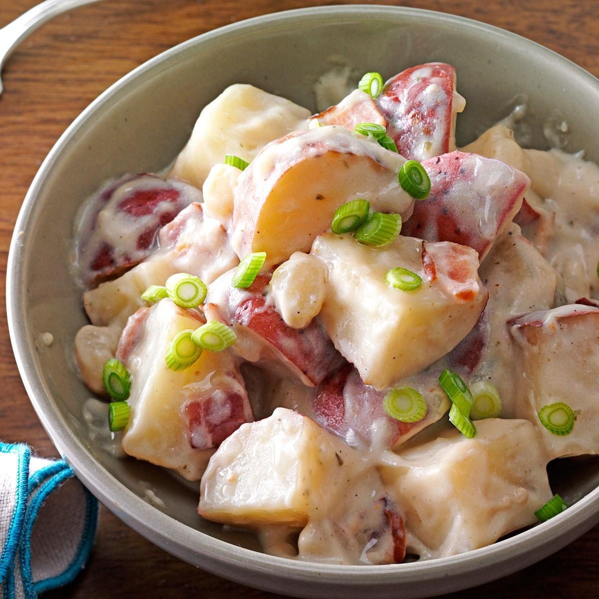 Potato salad tossed in creamy dressing, garnished with green onions, served in a gray bowl on a wooden table.