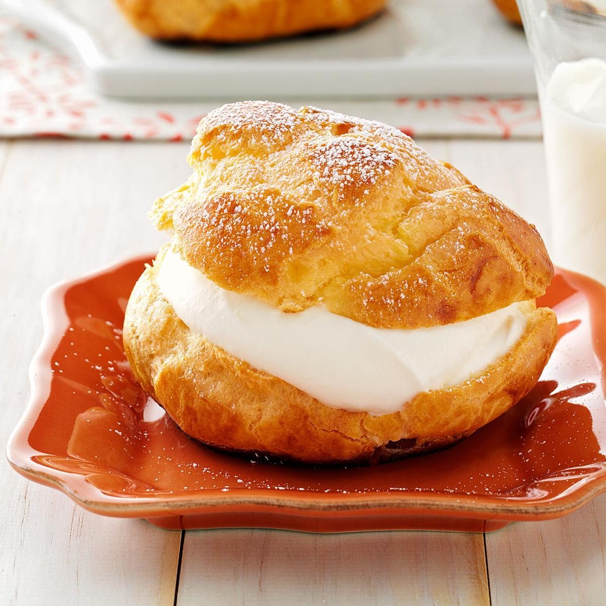 A cream puff sits on a red plate sprinkled with powdered sugar, placed on a wooden table.