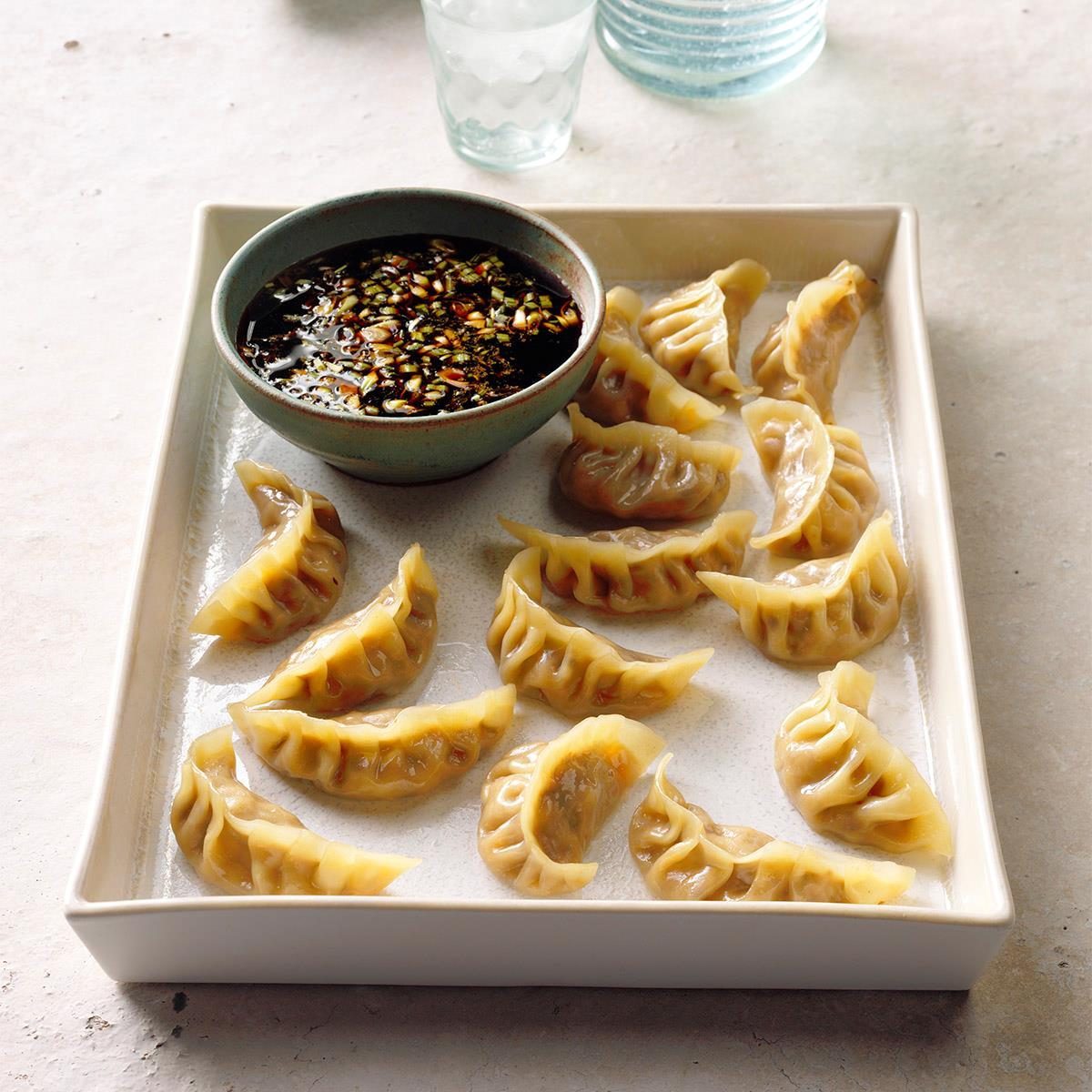 Dumplings arranged beside a dipping sauce bowl on a rectangular tray, placed on a light-colored tabletop.