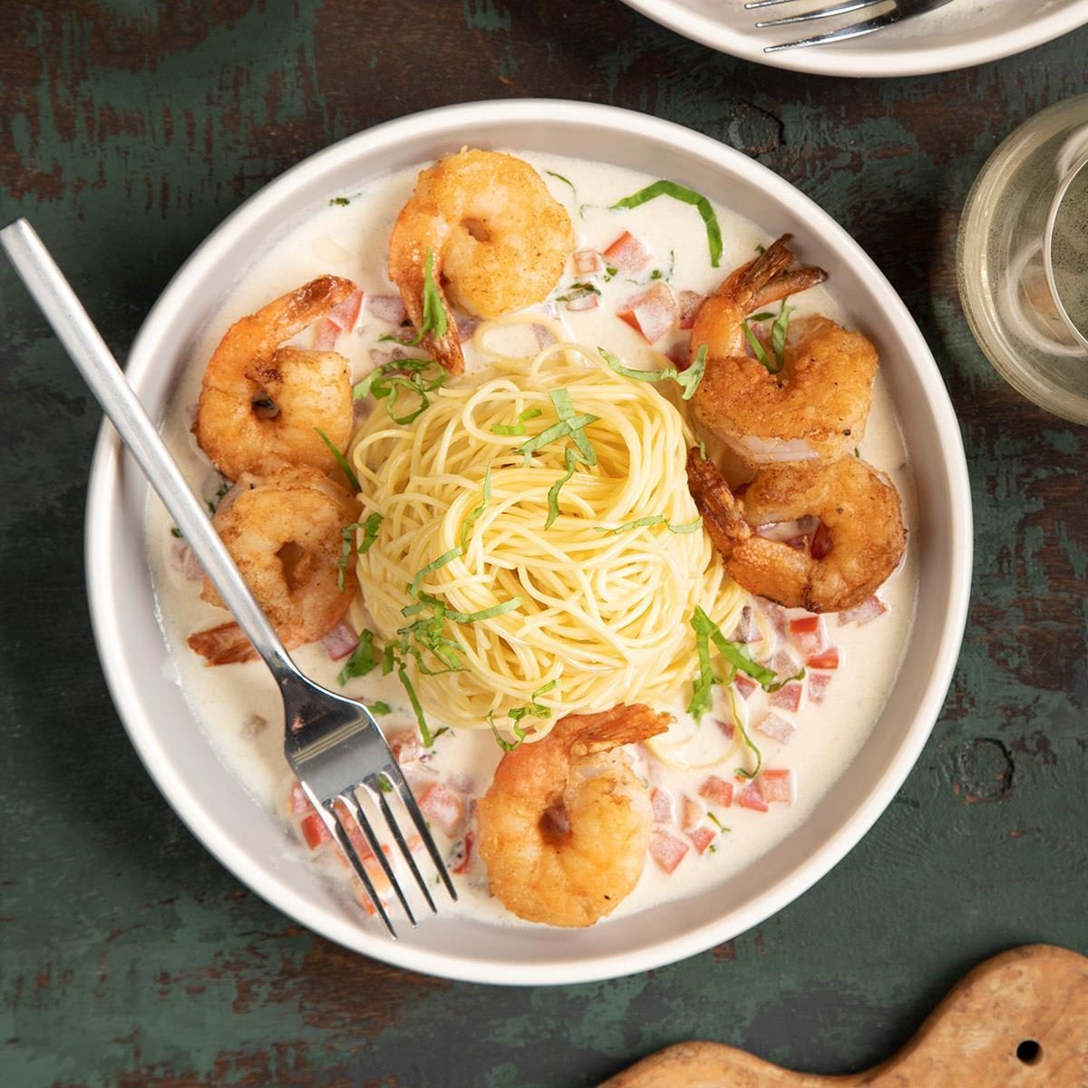 Pasta is arranged in a nest with shrimp and cream sauce, garnished with basil and diced tomatoes, on a white ceramic plate.