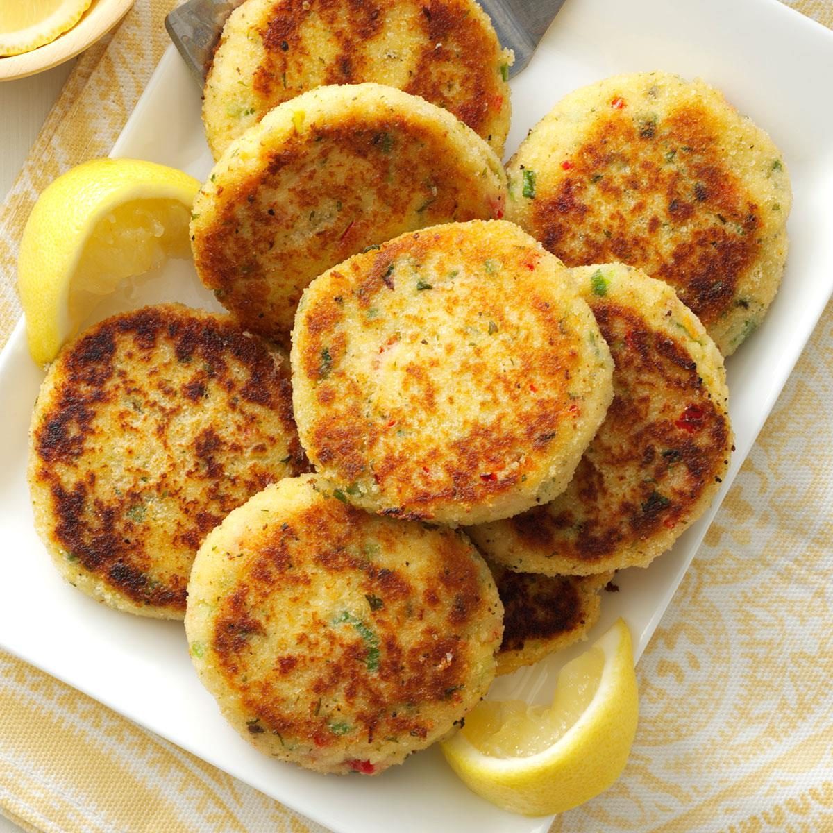 Golden patties rest on a white plate, garnished with lemon wedges, surrounded by a patterned yellow cloth.