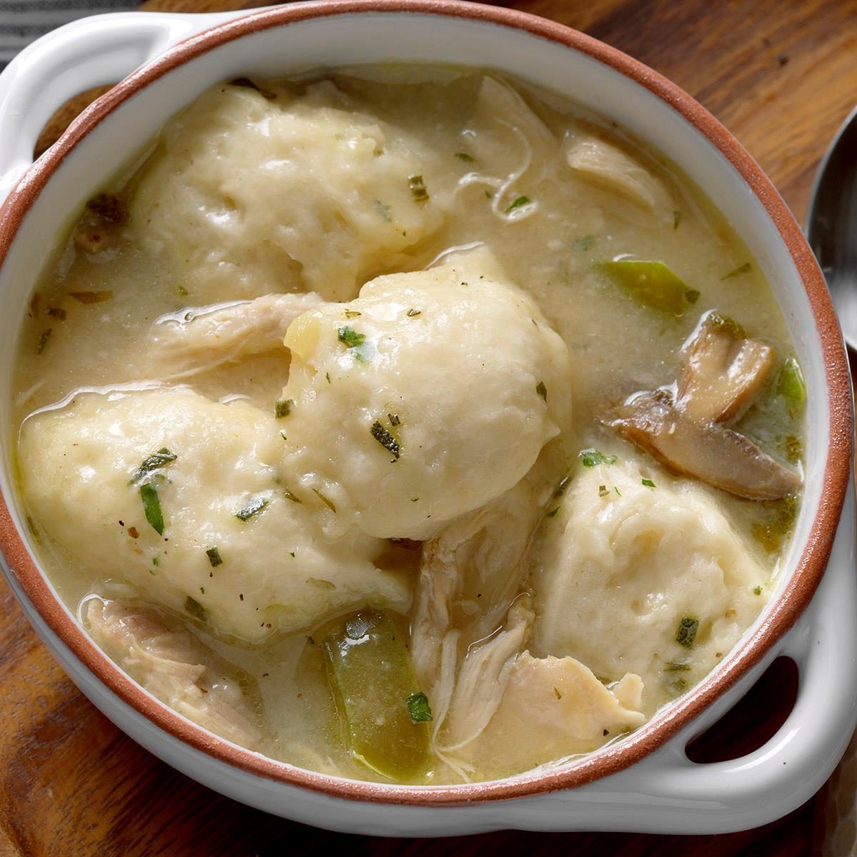 Dumplings float in creamy soup, garnished with herbs, inside a round ceramic bowl on a wooden table surface.