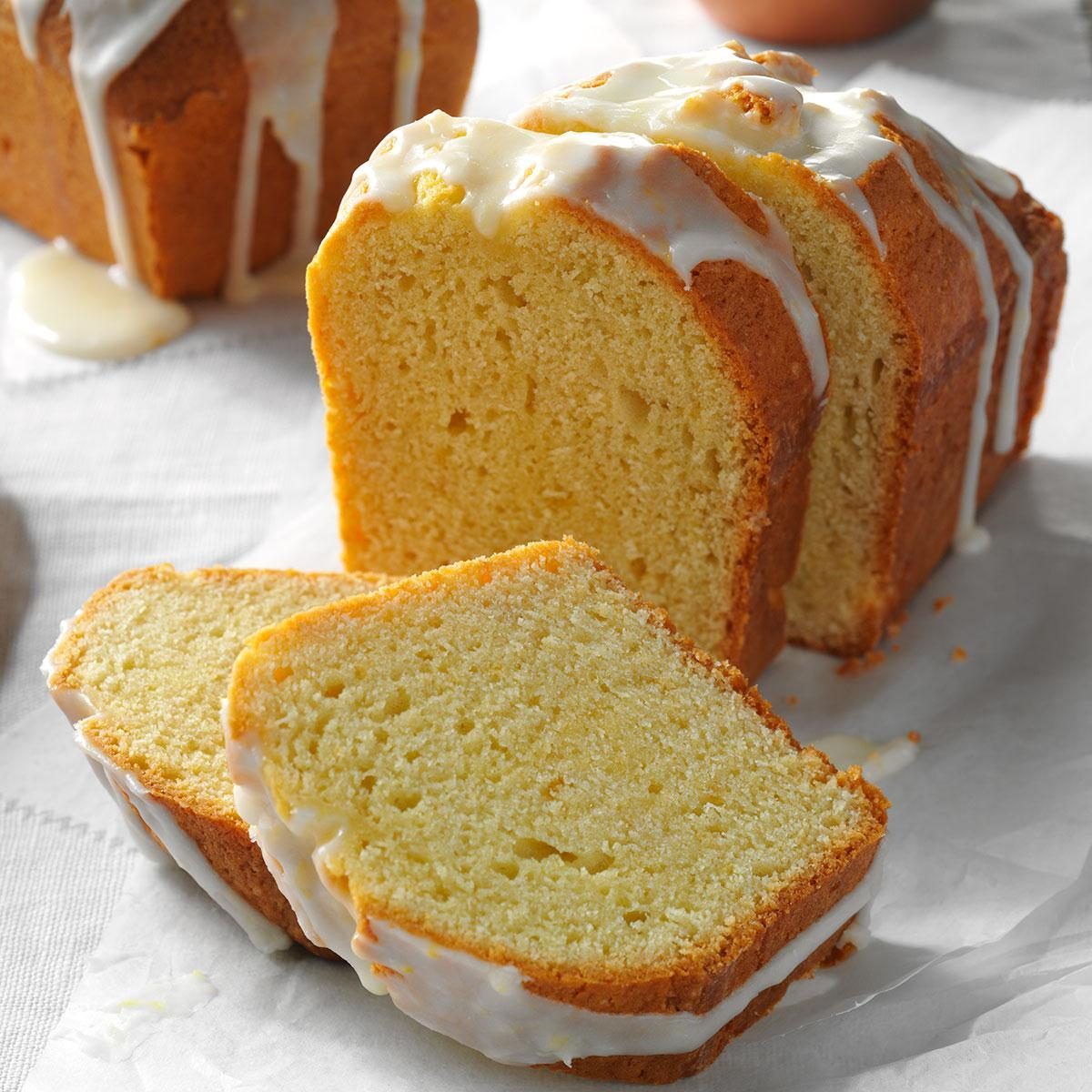 Lemon drizzle cake sits sliced on parchment paper, with icing visible and soft crumb texture, in a bright kitchen setting.