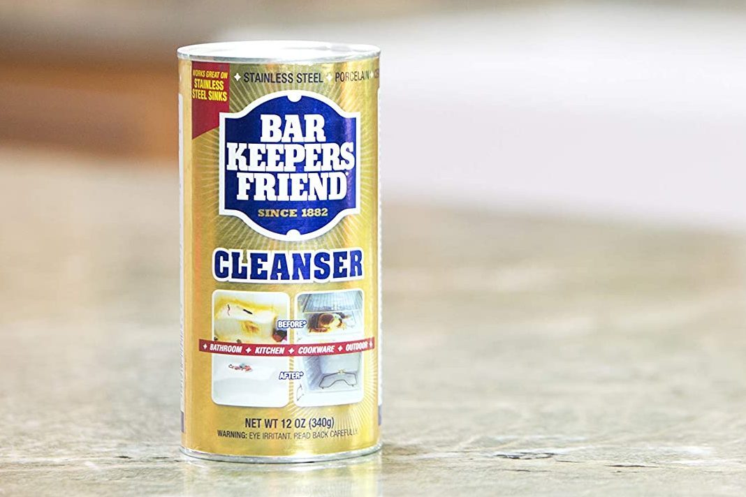 A cylindrical can of "Bar Keepers Friend" cleanser stands on a countertop, featuring cleaning uses for bathroom, kitchen, and cookware.