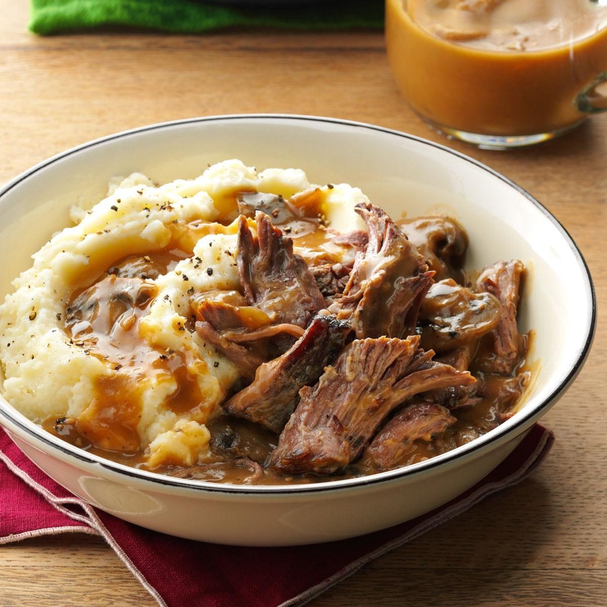 Mashed potatoes with gravy and shredded roast beef sit on a white plate over a red napkin, next to a cup of iced coffee.