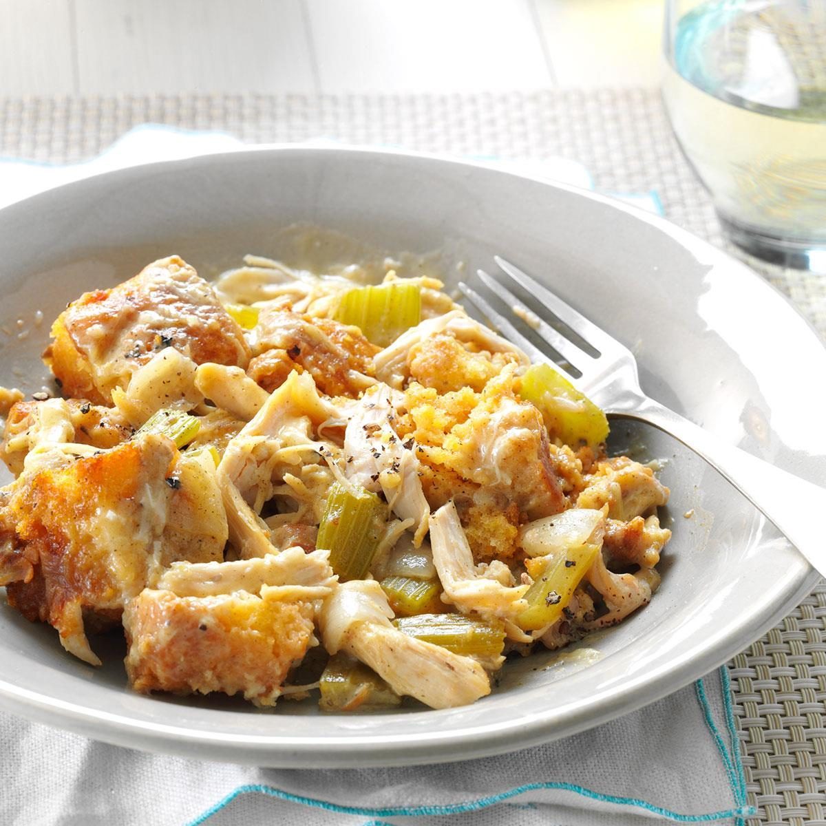 A dish of chicken, stuffing, and celery is served on a white plate with a fork, set on a woven placemat and white napkin.