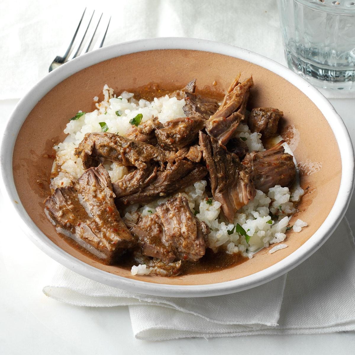 Bowl holds shredded beef over rice, garnished with herbs, on a white tablecloth beside a water glass and fork.