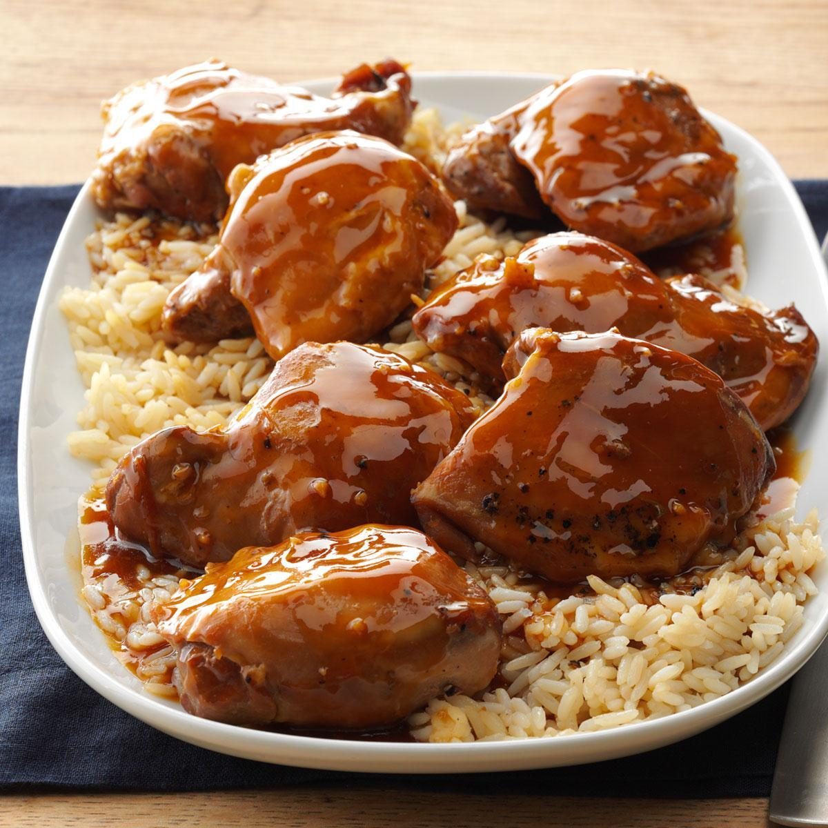 Glazed chicken rests on fluffy rice, served on a white platter, with wooden tabletop background.