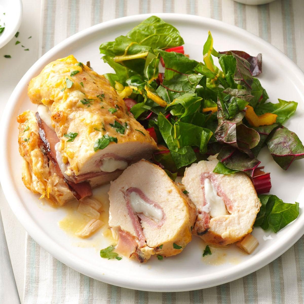 Stuffed chicken breast sliced, showing melted cheese and ham, is served on a plate with a side of fresh mixed greens.