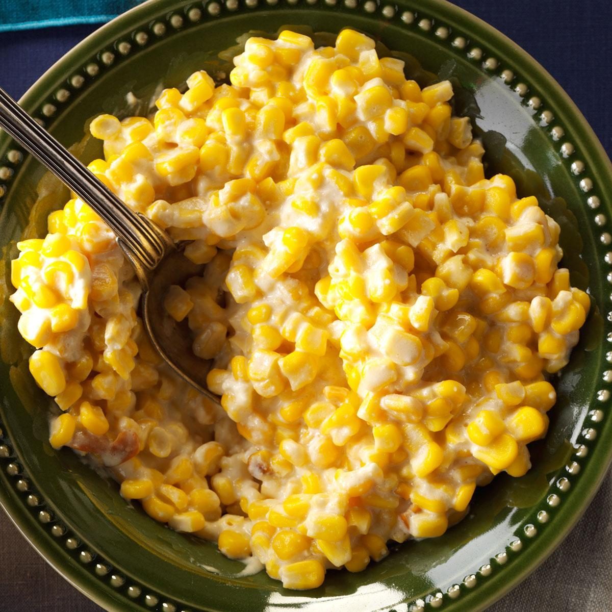 Creamed corn fills a green ceramic bowl with a spoon, creating a comforting, home-style meal atmosphere.