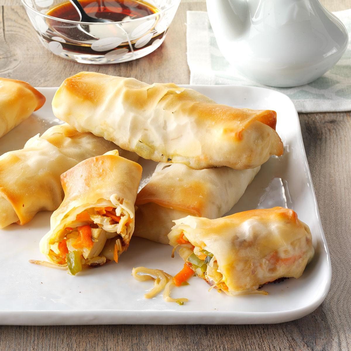 Egg rolls filled with vegetables sit neatly on a white plate; soy sauce is nearby in a small bowl.